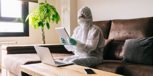 image of a woman in PPE and mask looking at a laptop